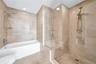Stone tile wall surfacing, glass-enclosed shower stall with a built-in bench, deep soaking tub, and polished chrome hardware