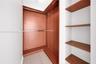 Built-in closet featuring wood-finish shelving, an L-shaped hanging rod system, and neutral wood-finish flooring