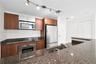 Kitchen featuring wood-finish cabinetry, stone countertops, stainless steel appliances, double-basin sink, and track lighting