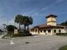 Commercial property exterior featuring stucco facade, multi-level tiled roofline, prominent architectural tower, and paved parking area with establish