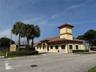Commercial property exterior featuring a tile roof, stucco facade, prominent tower element, and paved parking area
