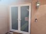 Double glass-panel doors with white frames, textured stucco exterior wall, and traditional wall-mounted lantern-style fixture