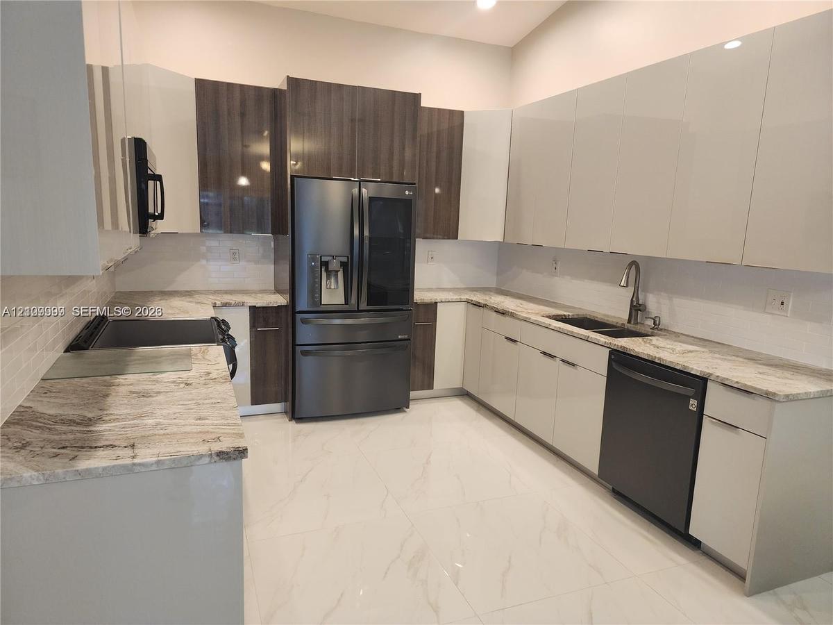 Kitchen featuring two-tone cabinetry with high-gloss finishes, stone countertops, large-format tile flooring, a double-basin undermount sink, and stai
