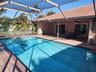 Screen-enclosed swimming pool with a concrete pool deck, covered patio, and tiled roof