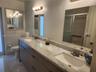 Dual-sink vanity featuring a stone-finish countertop, undermount sinks, contemporary cabinetry, wall-mounted lighting, and full-width mirrors