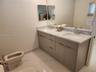 Dual-sink vanity with stone countertop, polished chrome hardware, large vanity mirror, and light-toned tile flooring