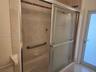 Tub and shower combination featuring a glass enclosure with decorative etching, integrated wall-mounted grab bar, built-in soap dish, and neutral cera