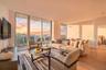 Floor-to-ceiling windows, wood-finish flooring, and a private balcony featuring a glass railing and expansive sky backdrop