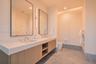Dual-sink floating vanity with light wood-finish cabinetry, crisp stone countertop, integrated vertical wall lighting, and natural stone flooring