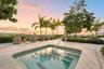 In-ground spa with stepped entry and metal handrail, surrounded by light-toned paver patio, lush perimeter landscaping, and mature palm trees