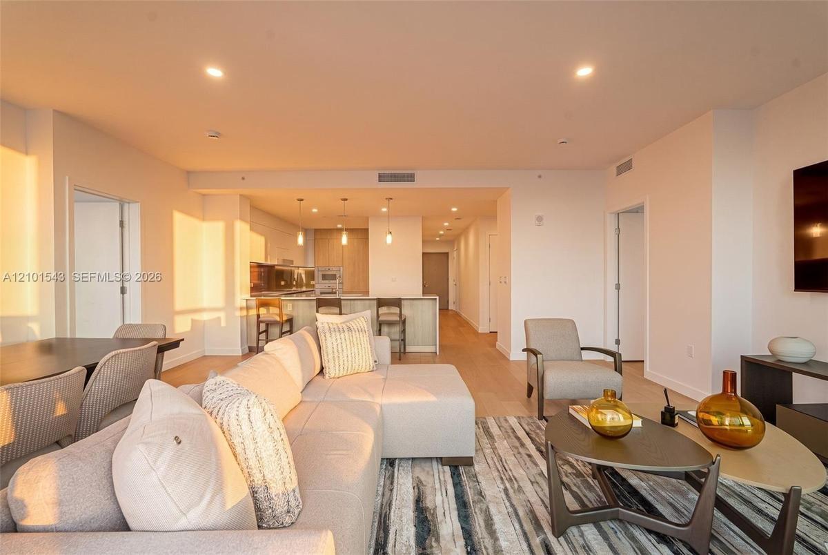 Open-concept living space featuring wood-finish flooring, recessed lighting, and a kitchen equipped with a stone-top island, built-in cabinetry, and m