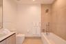 Bathroom featuring a wood-finish vanity, large-format neutral wall tile, integrated tub and shower combination with handheld fixture, and recessed lig