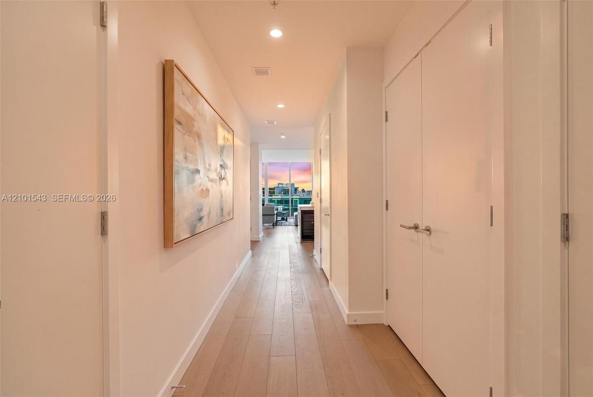 Interior hallway featuring wood-finish flooring, recessed ceiling lighting, and floor-to-ceiling double-door closets with satin-finish hardware