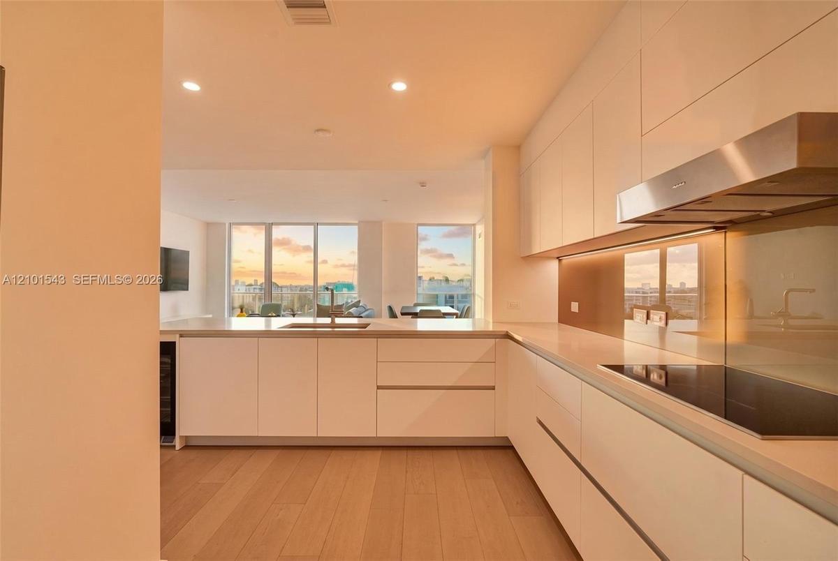 Contemporary kitchen featuring flat-panel cabinetry, light-toned wood-finish flooring, a stainless steel range hood, an integrated cooktop, and floor-