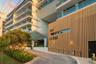 Contemporary architectural exterior featuring vertical wood-slat cladding, multi-level balconies with glass railings, and a covered porte-cochère entr