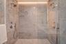 Walk-in shower featuring large-format stone wall tiling, mosaic stone flooring, dual shower heads with handheld sprayers, a frameless glass enclosure,