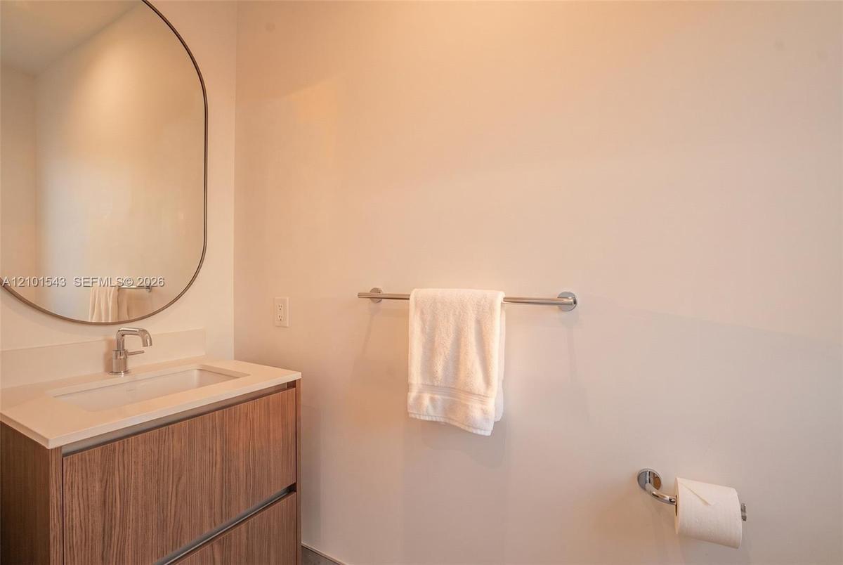 Wood-finish floating vanity with a stone-top integrated basin, polished chrome faucet, and oval wall-mounted mirror, complemented by matching chrome b