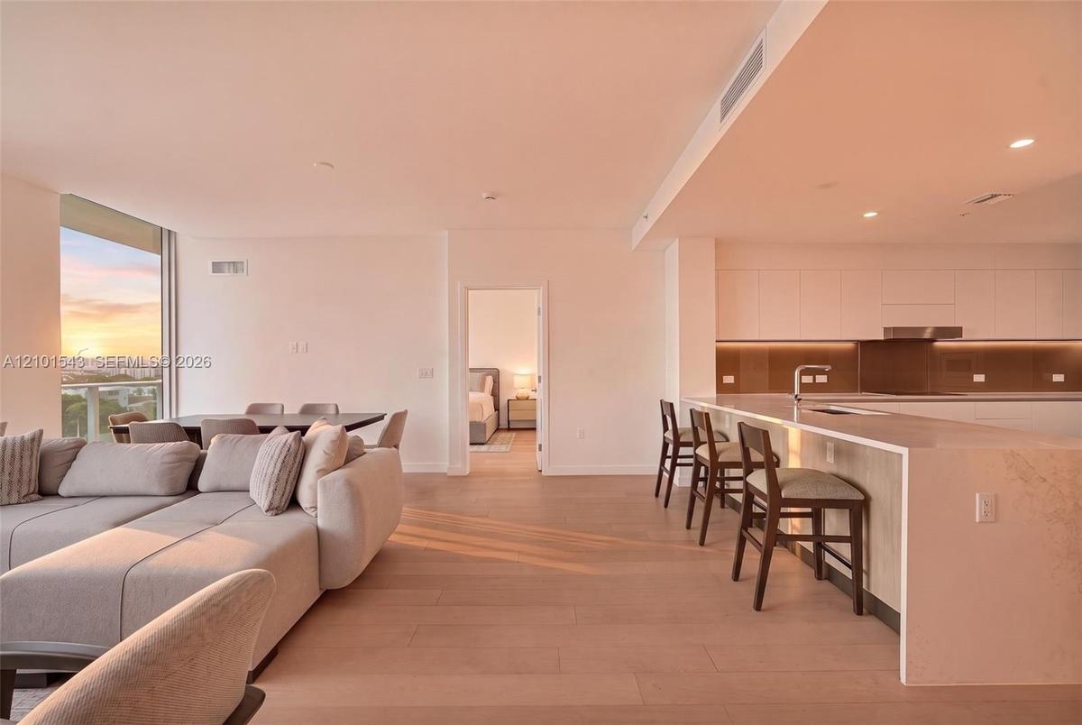 Open-concept interior featuring light wood-finish flooring, a kitchen with flat-panel cabinetry, a waterfall-edge countertop island, and recessed ceil