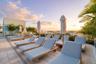 Rooftop terrace featuring light-toned stone tile flooring, perimeter landscaping with palm trees, and wide-reaching urban skyline scenery