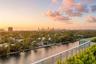 Elevated balcony featuring a glass panel railing, lush perimeter landscaping, and a panoramic perspective of the waterway and city skyline