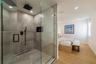 Walk-in shower featuring large-format stone-finish tile, glass enclosure, recessed wall niche, and matte black rainfall showerhead with handheld attac