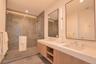 Floating dual-sink vanity with a solid surface countertop, glass-enclosed walk-in shower with stone tile surround, stone tile flooring, and integrated