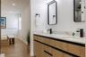 Modern vanity with wood-finish cabinetry, dual undermount sinks, stone-finish countertops, matte black fixtures, and rectangular mirrors