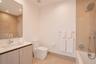 Bathroom featuring wood-finish cabinetry, a white rectangular sink, large-format tile surround, chrome wall-mounted fixtures, and a glass-enclosed soa