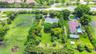 Aerial perspective of a sprawling lot featuring expansive grass acreage, dense mature trees, palm landscaping, and a circular driveway