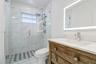 Bathroom featuring a wood-finish vanity with a stone countertop, an integrated rectangular sink, a frameless glass-enclosed shower with large-format t