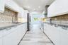 Kitchen featuring high-gloss white cabinetry, stone countertops, stainless steel appliances, a diagonal-patterned tile backsplash, and wood-finish flo