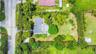 Aerial view featuring a expansive lot, perimeter landscaping, mature trees, and a paved driveway