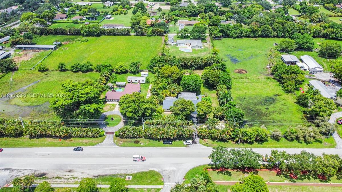 Aerial perspective of expansive acreage featuring mature trees, manicured landscaping, a circular driveway, and a gated entrance