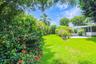 Spacious backyard featuring a manicured lawn, established perimeter hedges, mature trees, and a paved patio area