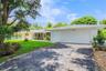 Single-story exterior featuring white stucco siding, a stone veneer accent wall, an attached two-car garage, and established landscaping
