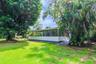Screen-enclosed porch featuring a concrete foundation, integrated ceiling fans, and a paved walkway, situated on a lawn with mature trees