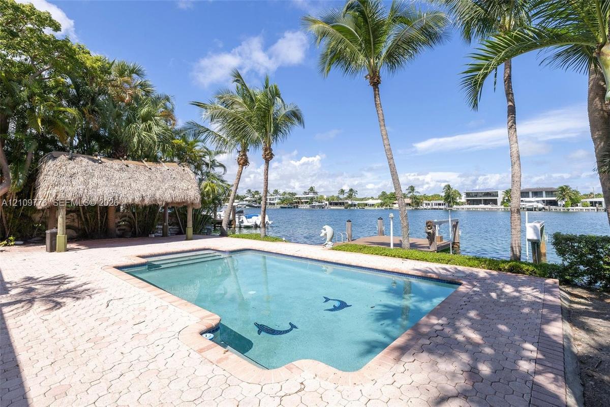 Waterfront pool area featuring a paver deck, thatched-roof tiki hut, tiled in-ground pool, and a private wooden dock