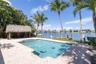 Waterfront pool area featuring a paver deck, thatched-roof tiki hut, tiled in-ground pool, and a private wooden dock