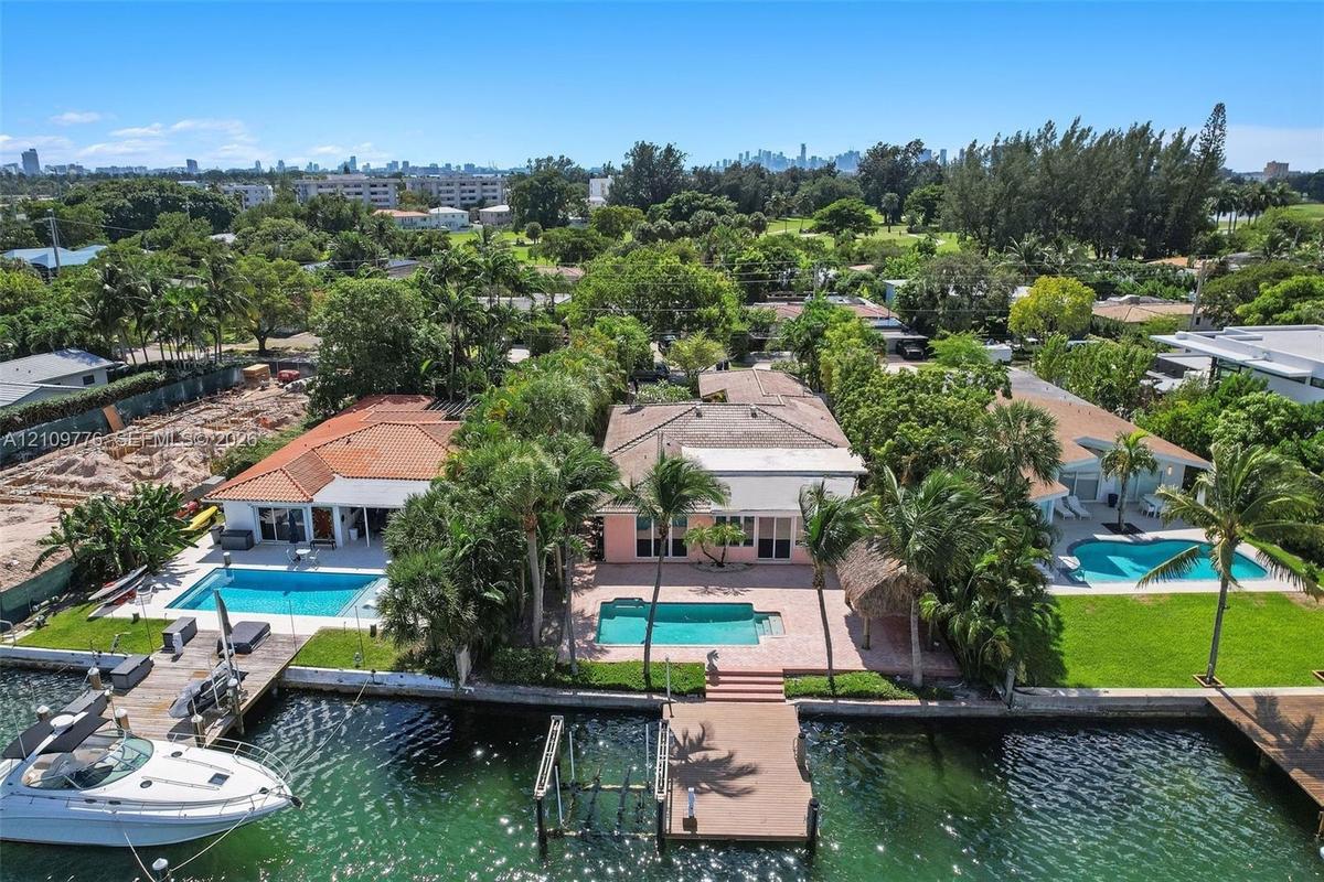 Waterfront property featuring a private swimming pool, paved patio, mature palm trees, and a wooden dock
