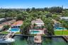 Waterfront property featuring a private swimming pool, paved patio, mature palm trees, and a wooden dock
