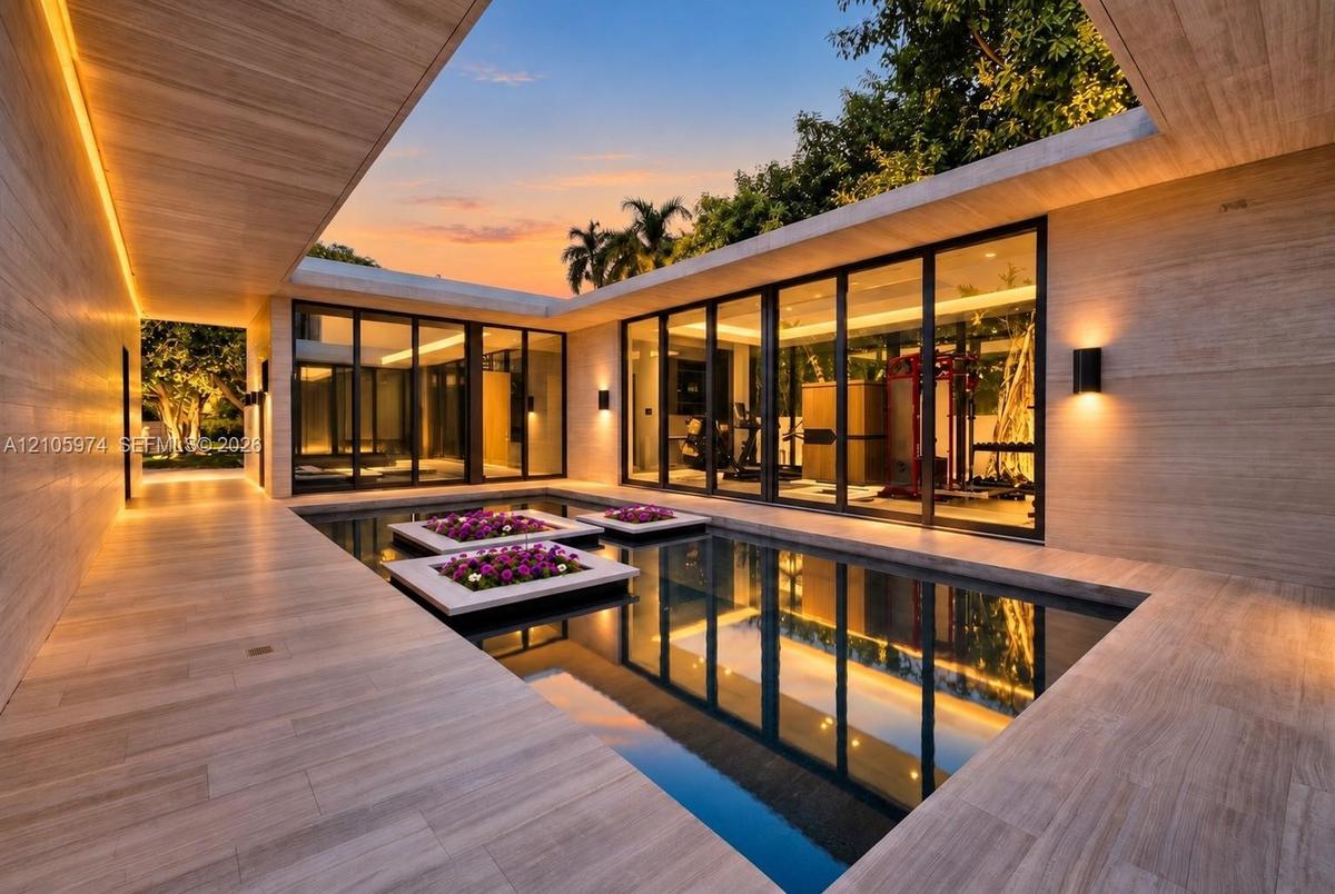 Central courtyard featuring a reflecting pool with integrated planters, floor-to-ceiling glass panel walls, natural stone-finish decking, and recessed