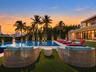 Outdoor living space featuring an inground swimming pool with stone tiling, synthetic grass lawn, perimeter hedges, and a glass-railed second-level ba