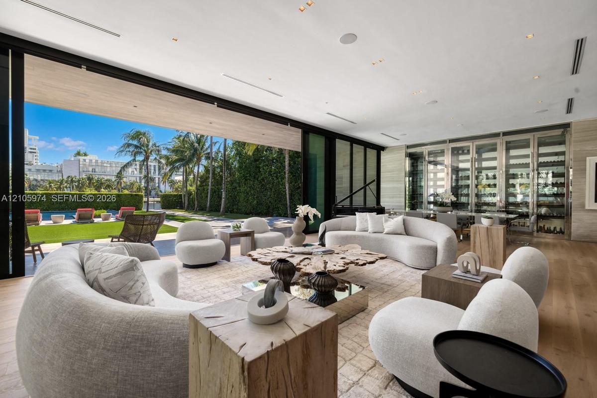 Floor-to-ceiling glass retractable wall, wide-plank wood-finish flooring, custom glass-enclosed wine storage, recessed lighting, and expansive stone w