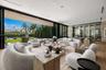 Floor-to-ceiling glass retractable wall, wide-plank wood-finish flooring, custom glass-enclosed wine storage, recessed lighting, and expansive stone w
