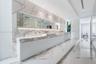 Large-format stone wall and floor tiling featuring prominent veining, integrated full-width vanity mirror with recessed lighting, and wall-mounted fau