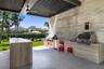 Covered outdoor kitchen featuring stone-clad surfaces, stainless steel built-in grill and beverage refrigeration, integrated faucet, and an overhead l