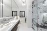Stone-surfaced vanity with an integrated basin, wall-mounted faucet, expansive wall-to-wall mirror, walk-in shower with glass enclosure, and decorativ