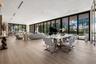Open-concept living space featuring wood-finish flooring, floor-to-ceiling glass panel walls, recessed linear lighting, and built-in ceiling speakers