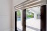 Dark-framed glass double doors featuring dual-layer roller shades, opening onto a covered patio with light-toned tile flooring, recessed ceiling light