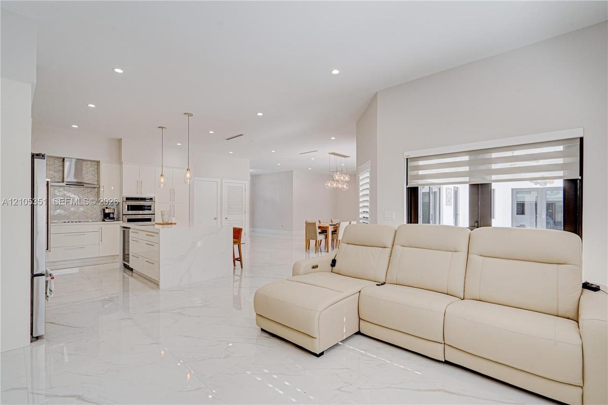 Open concept interior featuring high-gloss large-format tile flooring, stone-finish kitchen island, recessed lighting, and stainless steel built-in ap